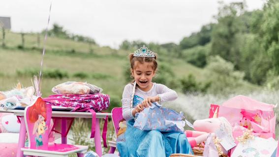 A young girl smiles in a blue and white dress smiles while opening gifts